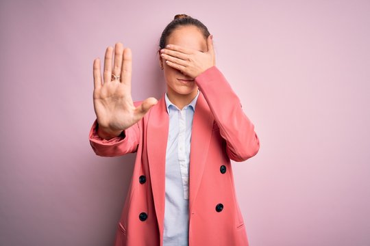 Young beautiful businesswoman wearing jacket and glasses over isolated pink background covering eyes with hands and doing stop gesture with sad and fear expression. Embarrassed and negative concept.