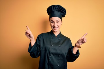 Young beautiful chef woman wearing cooker uniform and hat standing over yellow background smiling...