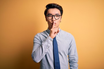 Young handsome chinese businessman wearing glasses and tie over yellow background asking to be...