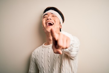 Young handsome chinese man injured for accident wearing bandage and strips on head laughing at you, pointing finger to the camera with hand over body, shame expression