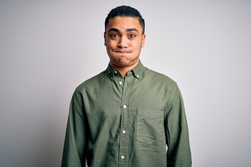 Young brazilian man wearing casual shirt standing over isolated white background puffing cheeks with funny face. Mouth inflated with air, crazy expression.