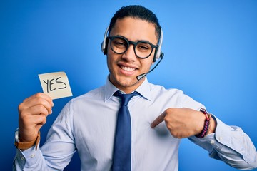 Young brazilian call center agent man holding reminder paper with yes message with surprise face...