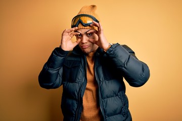 Young brazilian skier man wearing snow sportswear and ski goggles over yellow background Trying to open eyes with fingers, sleepy and tired for morning fatigue