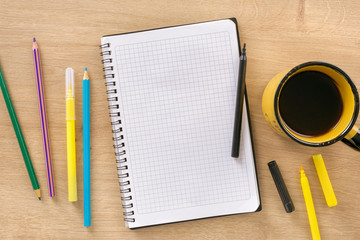 Office desk with epmty notebook, cup coffee, colored markers and pencils top view