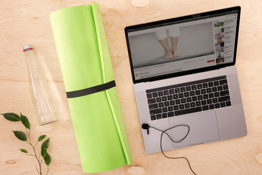 Online sports or yoga training concept Laptop with yoga mat, bottle of water and microphone on the table top view