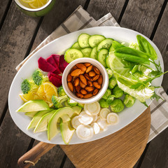 Plate of fresh healthy vegetarian food. Various vegetables and nuts in plate on wooden table top view