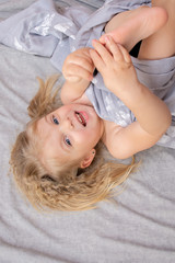 Portrait of a blue-eyed little girl with blond curly hair waking up in the morning on a gray bed laughing merrily.
