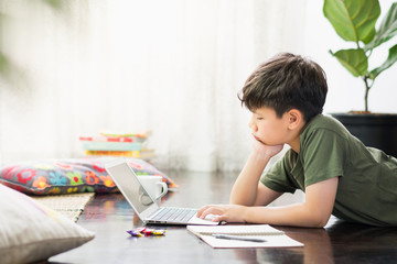 Smart looking Asian preteen boy use laptop computer at home study lessons through online learning, feeling tired with homework due to Covid-19 pandemic and social distancing measures