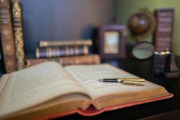 An Antique golden fountain pen, on an old book.  Magnifying glass, clock and more antique books in...