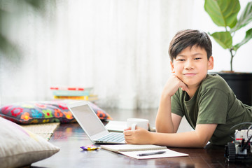 Smart looking Asian preteen boy lying on floor, smile with confidence and happiness, studying...