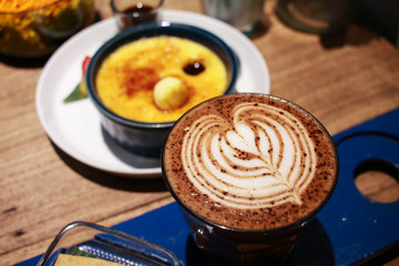 Cafe latte with latte art on a cup with Vanilla Crème Brûlée on the background.