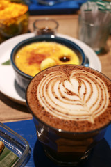 Latte art on a cup with Vanilla Crème Brûlée dessert on the background.