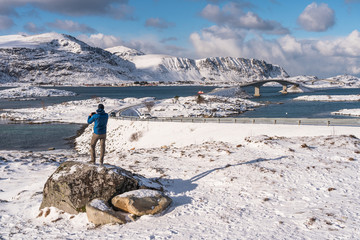 A traveller standing on rock and taking picture of Fredvang village in Lofoten island, Norway, Scandinavia