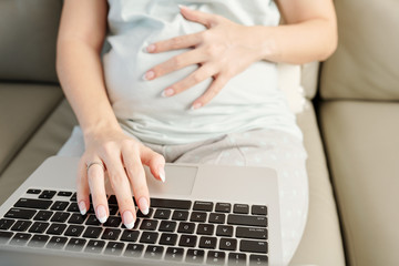 Fototapeta na wymiar Close-up image of pregnant woman with fresh manicure working on laptop from home
