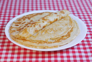 Delicious fried pancakes stack on a plate on a checkered tablecloth.
