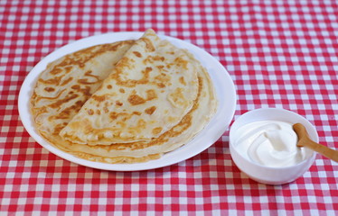Delicious pancakes Russian cuisine on a plate and sweet sour cream in a cup with a spoon.