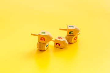 Dreidels - wooden symbol of Jewish holiday Hanukkah - on yellow background copy space