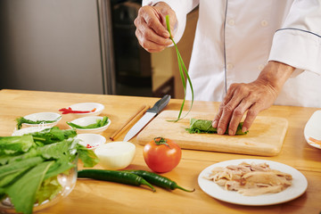 Man making delicious chicken roll and tying it with leek