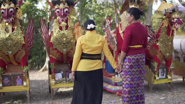 Two women holding hands heading to their family member's coffins in a traditional Balinese funeral ceremony. Last goodbye before cremation.