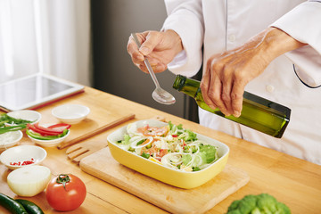 Cook adding table spoon of olive oil in bowl of fresh delicious salad
