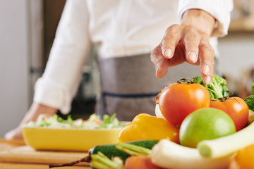 Close-up image of cook taking fresh ripe tomato from bowl to cut it for salad