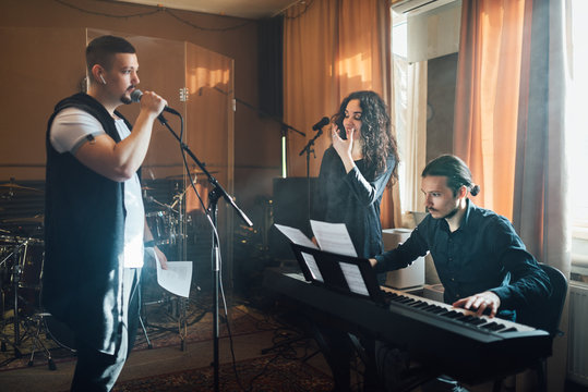man sings into microphone to accompaniment of electronic keyboards and teacher shows shape of mouth in vocal lesson