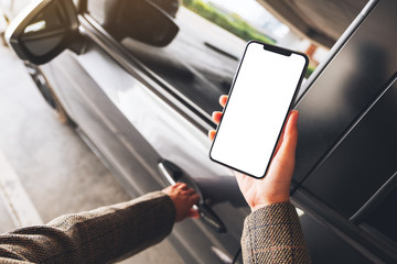Mockup image of a woman holding and using mobile phone with blank screen while opening the car door