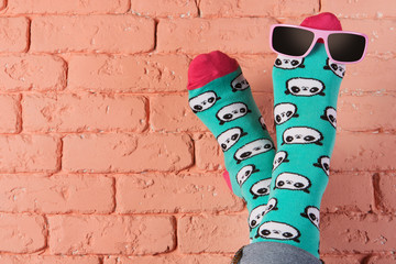 female legs in turquoise socks with a picture of panda faces, stick up, leaning on a brick wall, sunglasses on the leg, concept