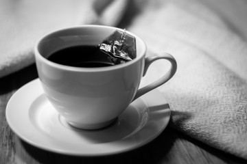 Cup of tea with tea bag dipping in hot water on wooden and cotton fabric background.