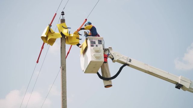laborer puts yellow sheets onto power line cables in basket
