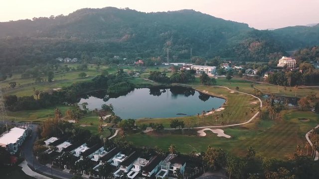Beautiful lake located on a golf course surrounded by houses and mountains at dawn, photo from a drone. In the lake the reflection of the sky. Great background for travel and golf advertising. 