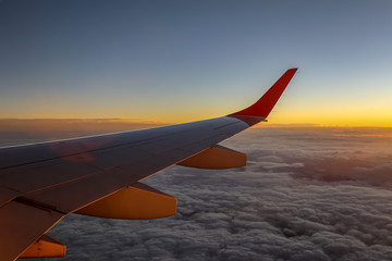 Fototapeta na wymiar Aircraft wing with fluffy clouds below and orange horizon during sunset