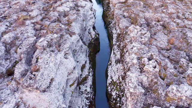 Narrow mountain river flowing through desolate pink rocky landscape. Stream bed cut deep into stones. Upstream of Cijevna (Cem) in Montenegro. Aerial footage.