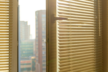 Open window with shutters in an apartment with blurred city views in the distance.