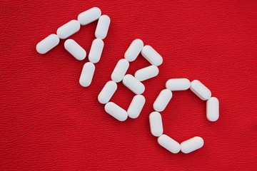 Alphabet made of pills on a red background. Abc from drugs. Vitamins White pills without an...