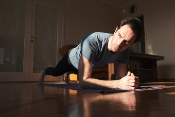 Sport, fitness and healthy lifestyle concept - man doing plank exercise at home