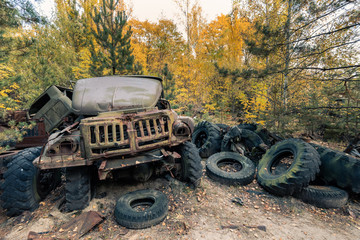 Front of broken down military truck with pile of old tires in overgrown police compound in Pripyat,...