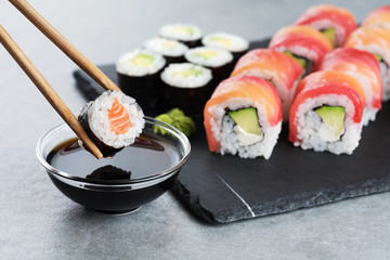 Sushi maki with salmon and avocado, sushi philadelphia, soy sauce and wasabi. Chopsticks taking portion of sushi roll. © vitals