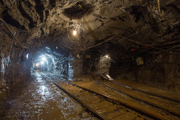 Fototapeta na wymiar Underground gold mine tunnel with rails two ways and light