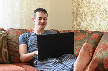 Young attractive man working from home living room sitting on sofa with laptop. Remote work concept