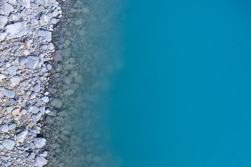 Aerial top view of turquoise lake and rocks abstract background at Tekapo, New Zealand