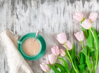 Green cup of tea with cream on a gray wooden table. Nearby is a bouquet of pink tulips and a tissue napkin. Place for text. Flat lay. View from above.