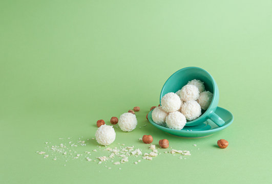 The green cup is turned on its side. From it fall Raffaello sweets. Near a cup of hazelnuts and wafer crumbs. Green background. Place for text.