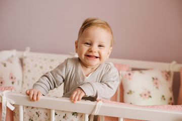 Cute little baby girl standing in cot after sleeping.