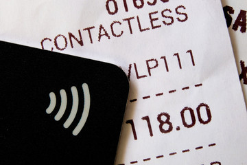 A contactless payment icon symbol on a credit card on top of sales receipts showing goods were paid using contactless method or wave or near-field communication technology. Closeup macro view.