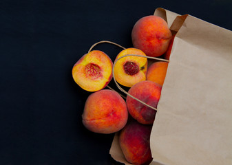 Fototapeta na wymiar juicy peaches spilled out of the bag. paper bag. cut peach. open peach. juicy summer fruit. peach on a black background. copy space. 
