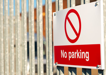 Close up view of a red & white No Parking sign attached to a metal security fence, at an industrial trading estate in Colliers Wood, London, UK.
