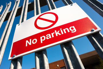 Obraz premium Low angle view, of a red & white No Parking sign attached to a metal security fence, at an industrial trading estate in Colliers Wood, London, UK