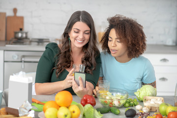 Girlfriends looking at a smartphone at a table with vegetarian products.