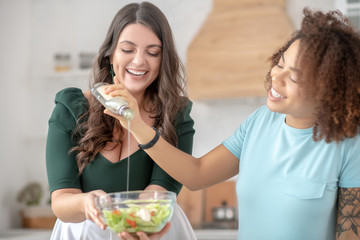 Obraz na płótnie Canvas Two women add salad oil in vegetable salad.